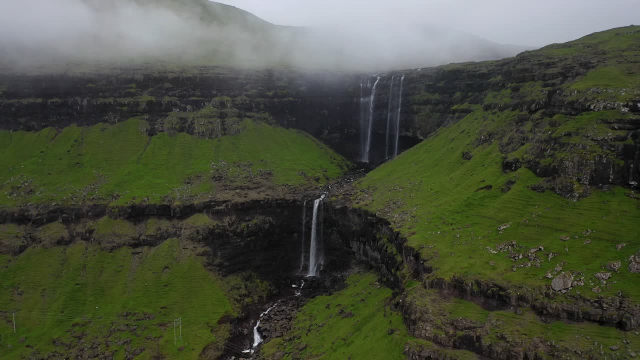 catarata de fossá con línea eléctrica sobre el río en las nubes de las islas feroe, retiro aéreo