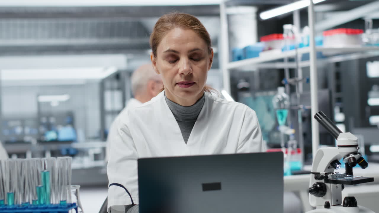 Scienziata stanca con mal di testa mentre lavora al laptop in laboratorio.