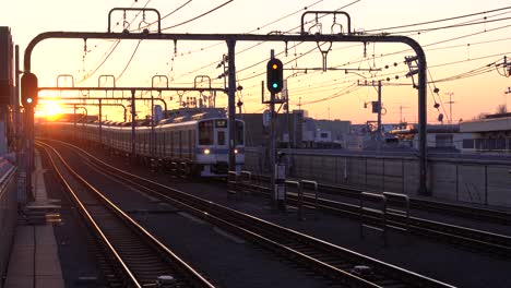 tren circulando por las vías que se acercan a la estación en japón con una hermosa puesta de sol en el fondo - plano general