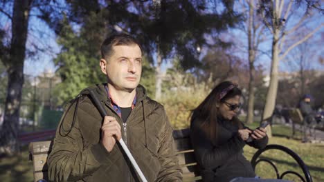 The-blind-man-in-the-coat-is-sitting-on-a-bench-under-a-tree-in-the-autumn.