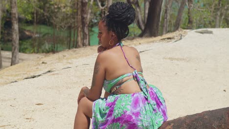 Una-Mujer-Joven-Está-Parada-En-Lo-Alto-De-Un-Acantilado,-Con-Su-Vestido-Ondeando-Al-Viento-Mientras-Mira-Hacia-La-Playa.