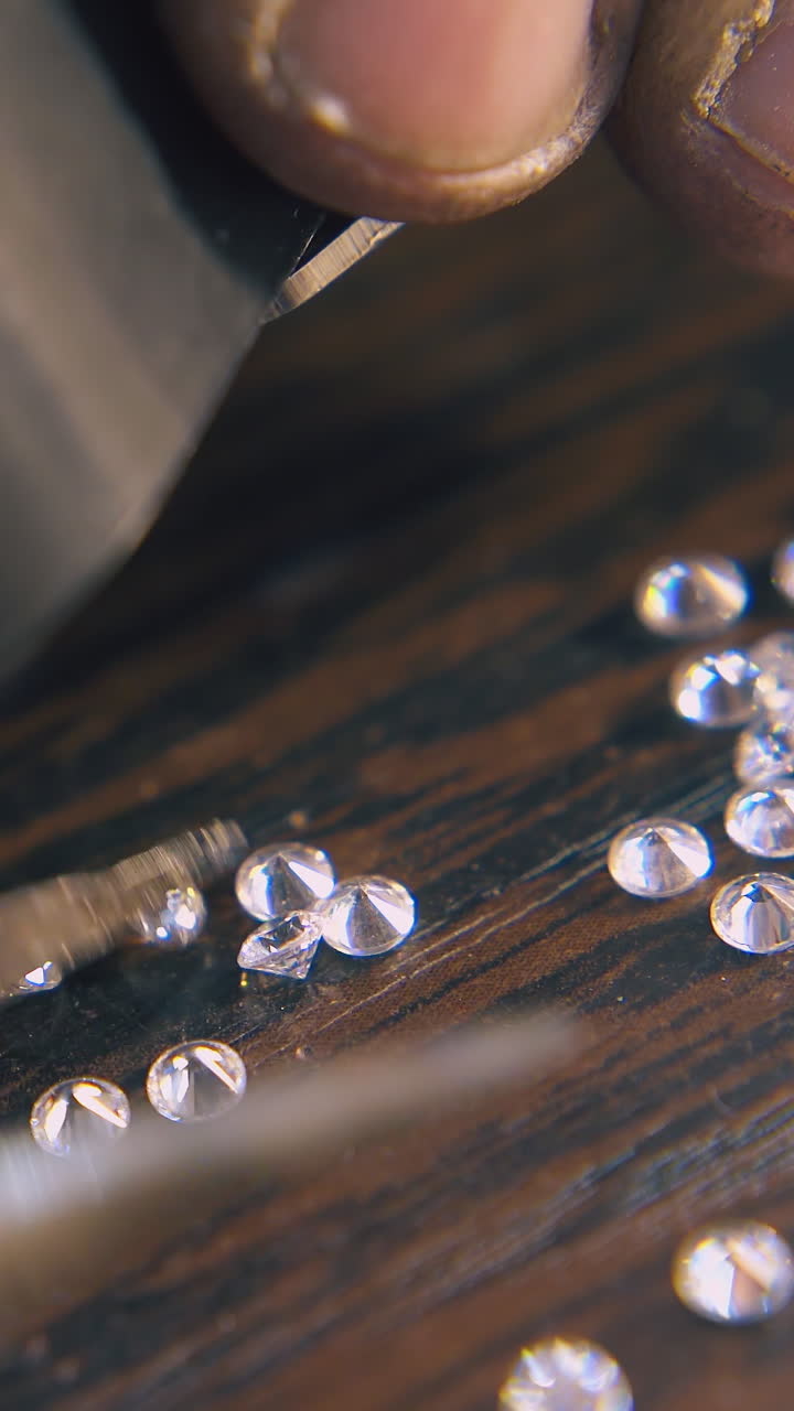 CU: professional jeweler chooses beautiful diamonds with tweezers looking through magnifier glass at wooden table closeup