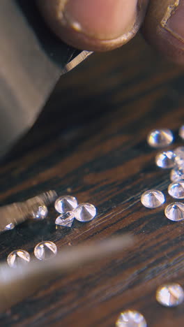cu: professional jeweler chooses beautiful diamonds with tweezers looking through magnifier glass at wooden table closeup