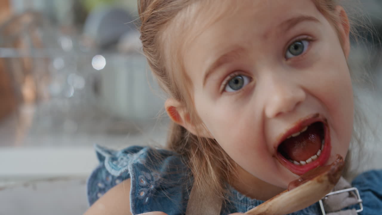 una bambina felice che lecca il cucchiaio assaggiando delizioso budino al cioccolato godendo di dolci casalinghi in cucina 4k