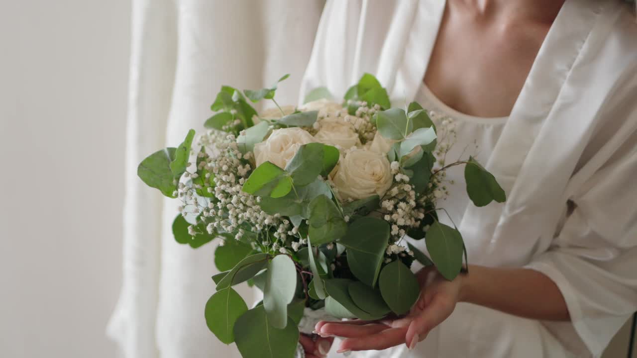 bride delicately holds a bouquet of white roses and green leaves in a softly lit room in Porto
