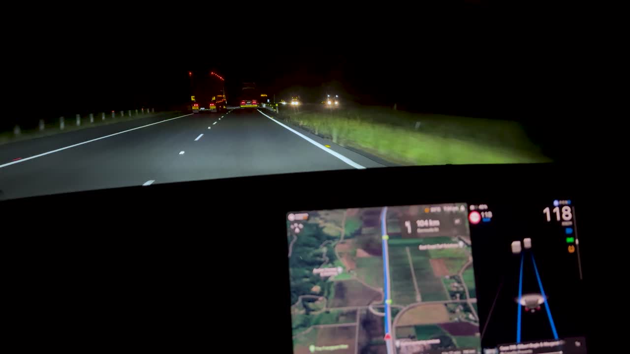 Car drives on dark highway at night, illuminated by headlights, dashboard navigation screen visible throughout