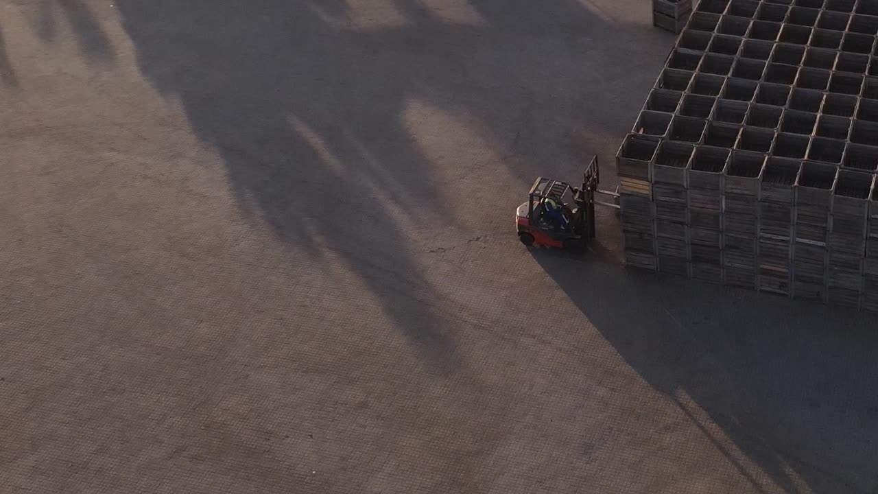 An aerial view of a forklift carrying pallets to load onto a pile of pallets and then reversing away