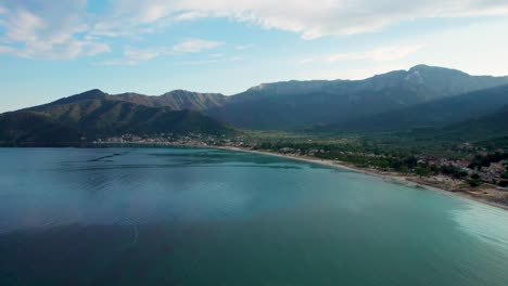 Side-Aerial-View-Of-Golden-Beach-At-Sunset-With-Sun-Rays-Bursting-Through-Towering-Mountain-Peaks,-Beautiful-Beachfront-And-Lush-Green-Vegetation,-Vivid-Colors,-Thassos-Island,-Greece,-Europe