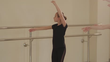 a group of young ballet students in black dancewear practicing positions in a spacious ballet studio with wooden flooring and wall-mounted barres. focused expressions and synchronized movements.