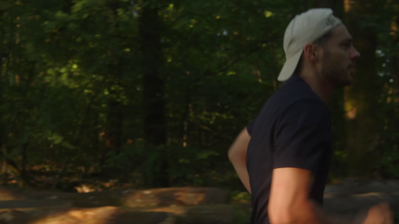 rastreando a un joven atleta moderno corriendo en cámara lenta a través del bosque