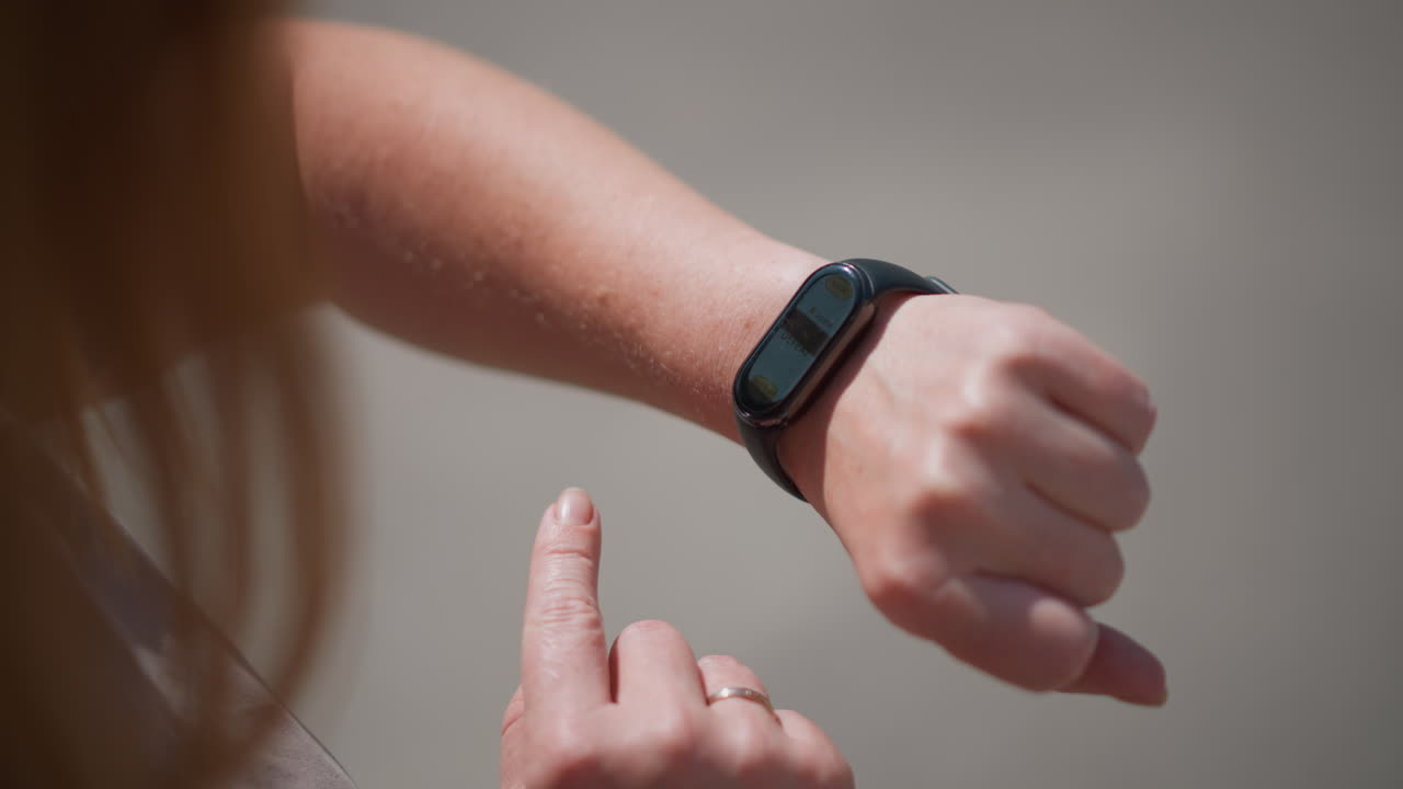 Top close up of white lady tapping smartwatch screen outdoors under sunlight, reflection on display showing focus and interaction, capturing concept of modern lifestyle and wearable technology