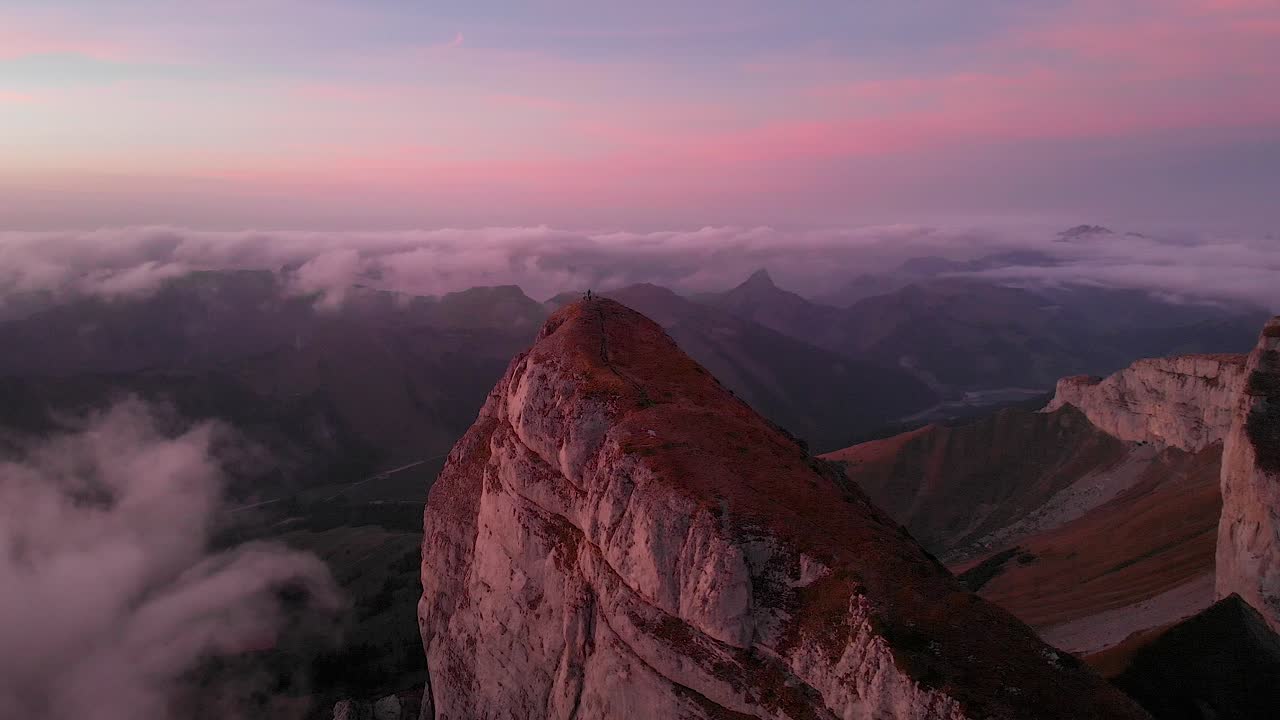 Aerial flyover around Tour d'A&iuml; in Leysin, Vaud, Switzerland during a colorful autumn sunset with hikers and climbers enjoying the view above clouds with Tour de Mayen in the background