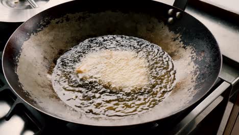 Homemade-fresh-raw-uncooked-spring-rolls-tossed-in-hot-frying-pan-of-boiling-oil-and-stirred-with-metal-tongs,-static-close-up