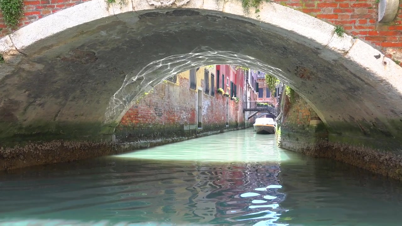 Barca che passa sotto un ponte storico in mattoni a Venezia