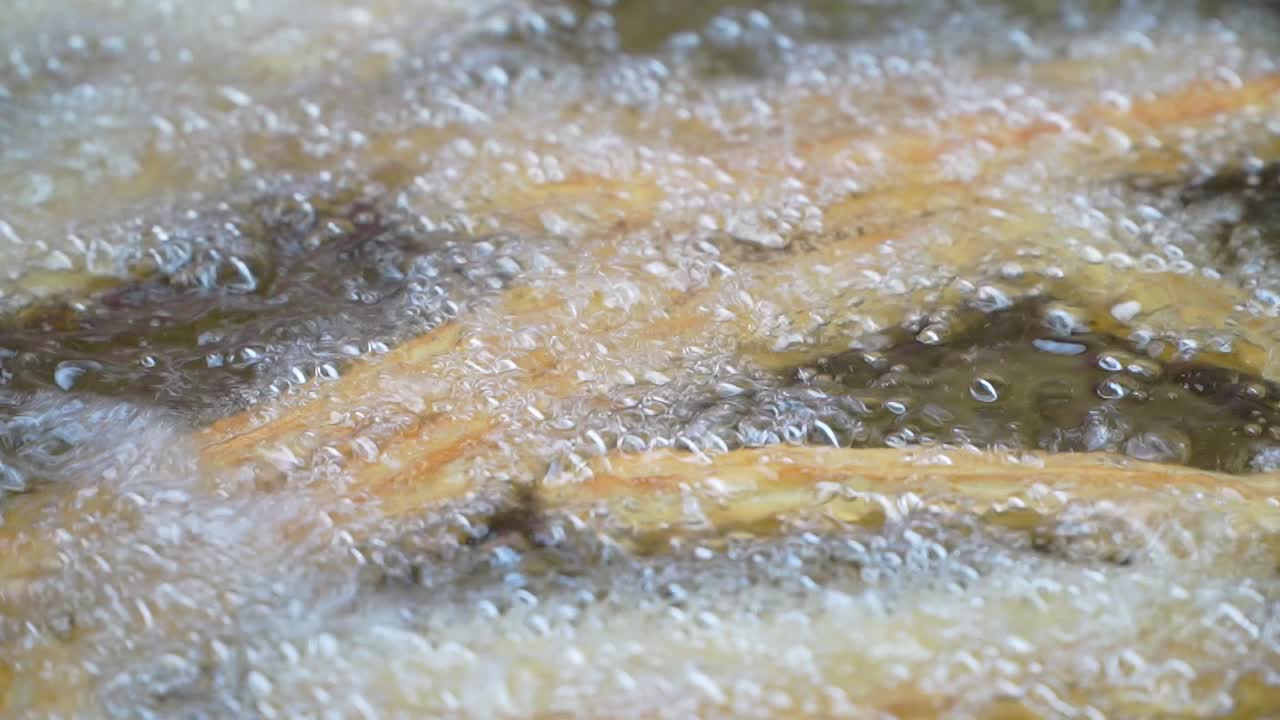 Closeup of churros being cooked in boiling oil.