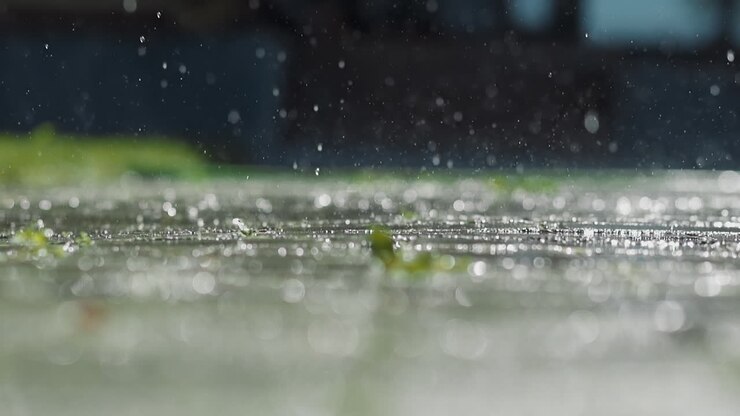 Clear drops of rain water fall down on paved road macro