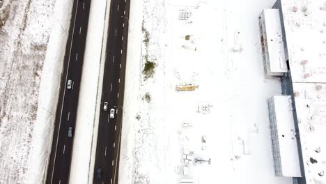 Commercial-building-construction-site-covered-in-white-snow-near-highway-road-with-many-cars,-aerial-view