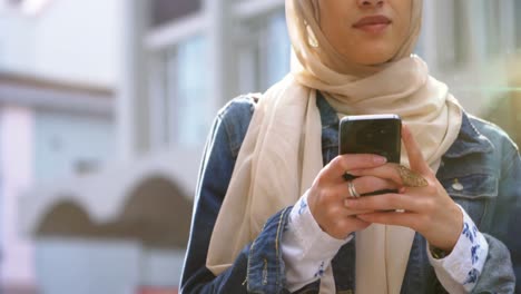 Animation-of-smiling-asian-woman-in-hijab-using-smartphone-over-cityscape