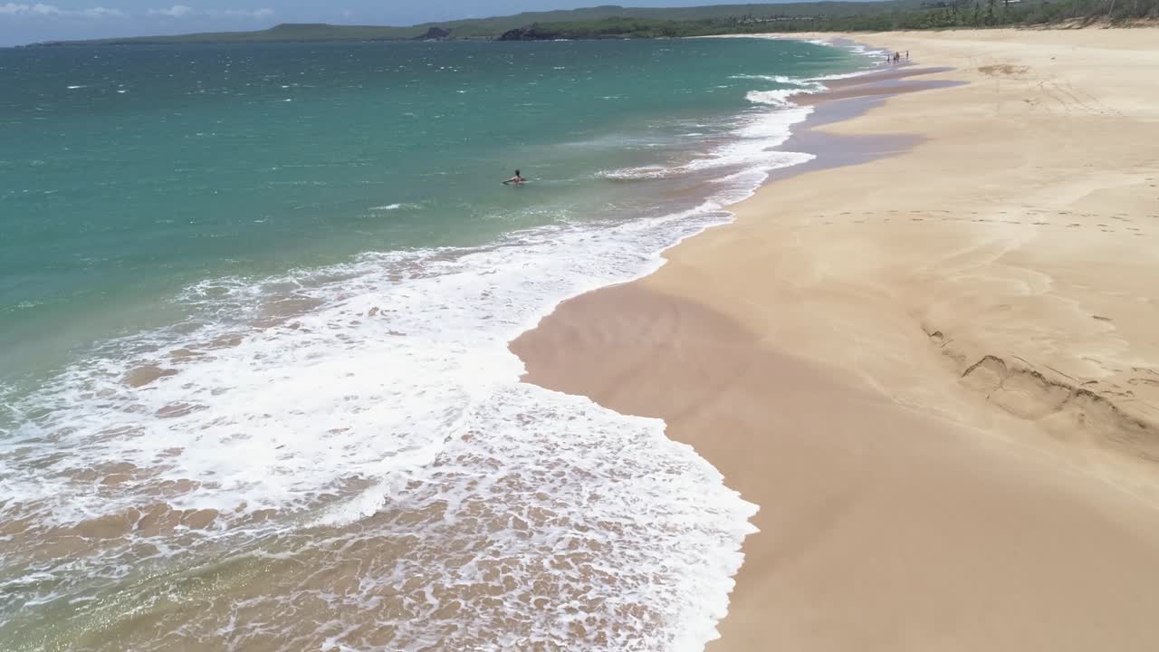 giovane che gioca e viene colpito dalle onde sulla spiaggia di papohaku a maui hawaii in una luminosa giornata di cielo blu