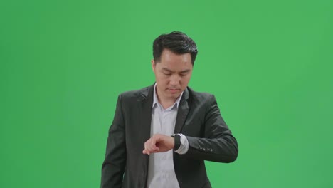 asian business man walking while looking at watch and run on green screen chroma key