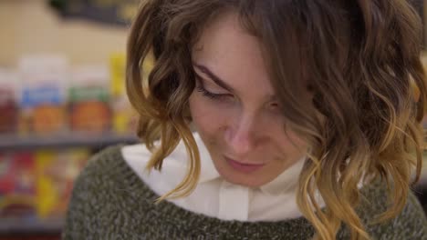 young curly haired woman doing grocery shopping at the supermarket, she is reading a product label and nutrition facts on a box with cheese. footage from the shelf, exremely closeup of face