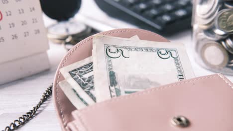 money in a pink wallet with calendar, clock and calculator in the background