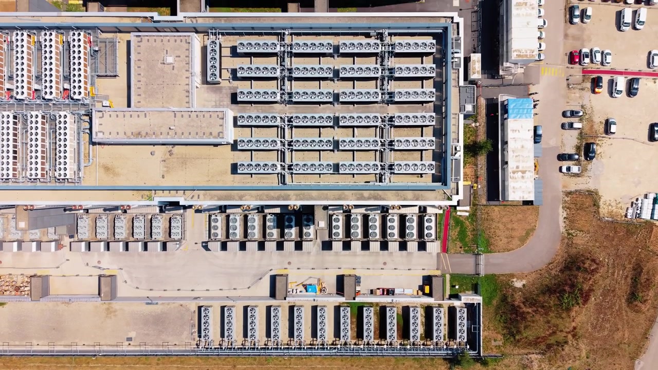Drone advances forward in top down view over data center rooftop cooling units