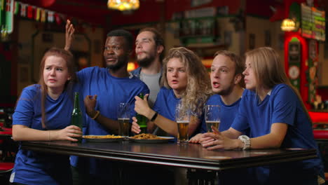 a group of friends of fans in blue t-shirts excitedly emotionally watch the match and rejoice at the goal scored jump and shout emotionally. celebrate and celebrate a goal scored by chewing with beer.