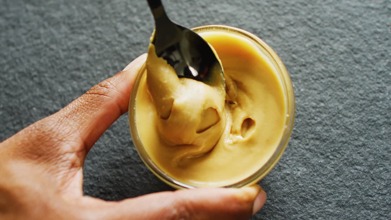 Video of close up of hand with peanut butter on gray background