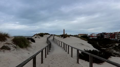 sandy wooden path leads to costa nova beach with barra lighthouse, cloudy sky over coastal dune