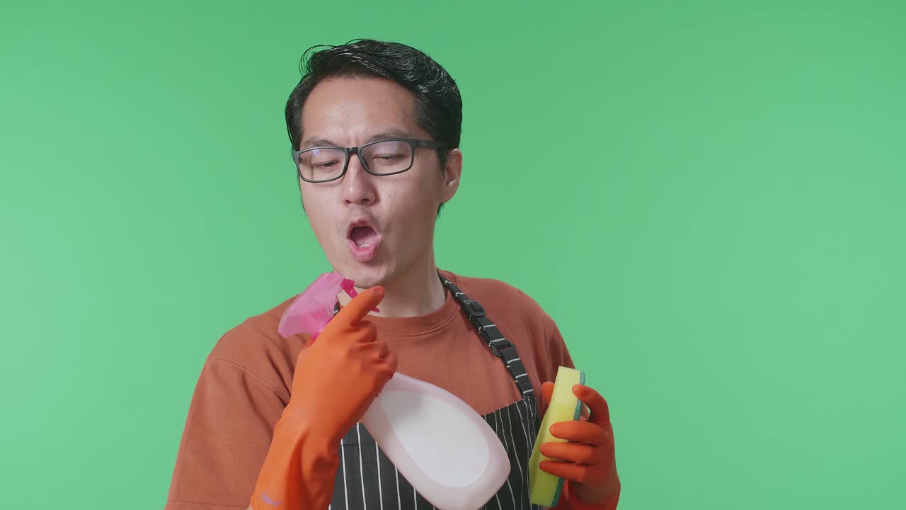 녹색 스크린 스튜디오에 서 있는 동안 총으로 불기 전에 아프론 스프레이를 가진 아시아 남성 집주인의 클로즈업