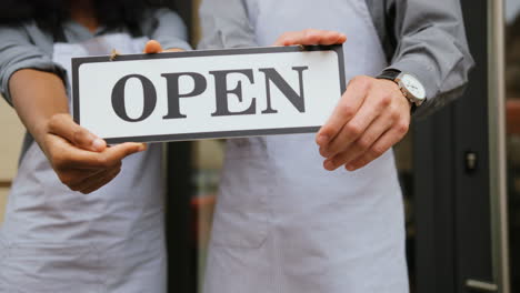 Close-up-view-of-caucasian-waiter-and-african-waitress-hands-holding-a-signboard-open"-outside-of-coffee-shop"