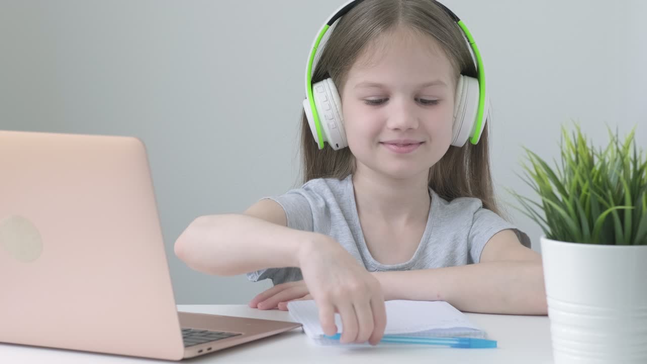 Happy school girl wearing wireless headphones studying online at virtual class with teacher tutor
