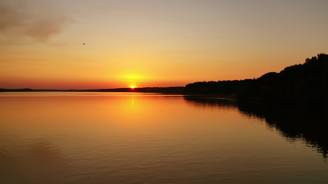 River at the setting sun. Beautiful orange sunset over the evening river. Birds flying over the water. Camera moves back. Aerial view.
