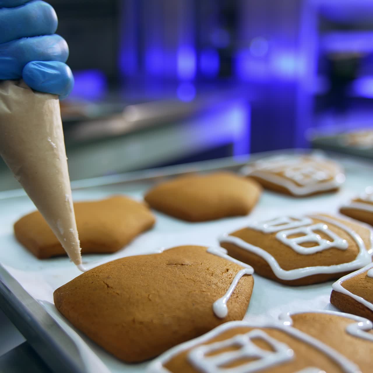 Putting white icing on the gingerbread cookies. Close up. Manufacturing sweet desserts at confectionary factory. Blurred background