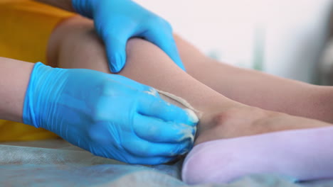 two girls in a beauty salon master in a bathrobe and gloves doing the procedure to remove hair on the legs with a sugar mixture