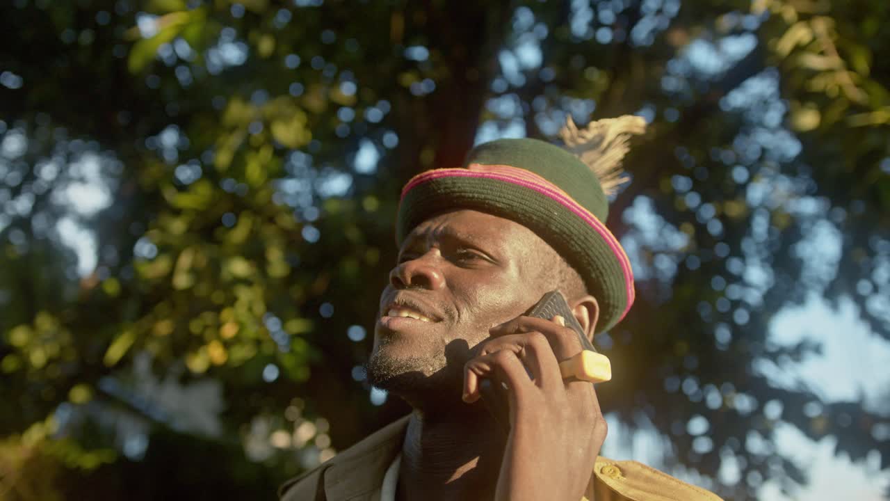hombre africano con sombrero de pluma hablando por teléfono móvil en el bosque de uganda