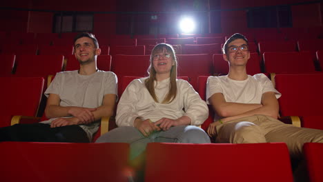 three friends in the cinema hall, having fun watching a film, front view