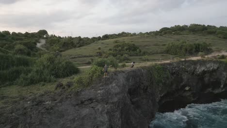 man and motorcycle stand atop steep rocky cliffs on tropical coastline