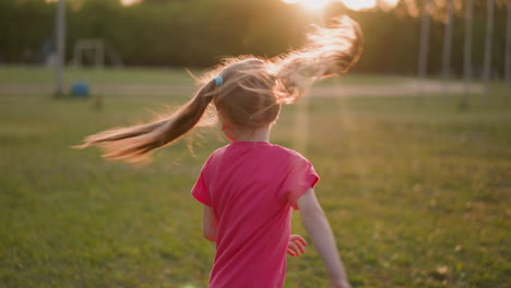 funny girl shakes long ponytails on lush field at sunset