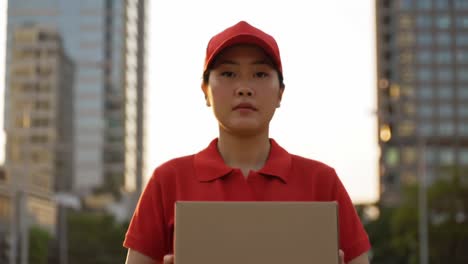 a determined delivery person stands in an urban landscape at sunset, holding a cardboard box, showcasing dedication and commitment to their role in logistics and transport