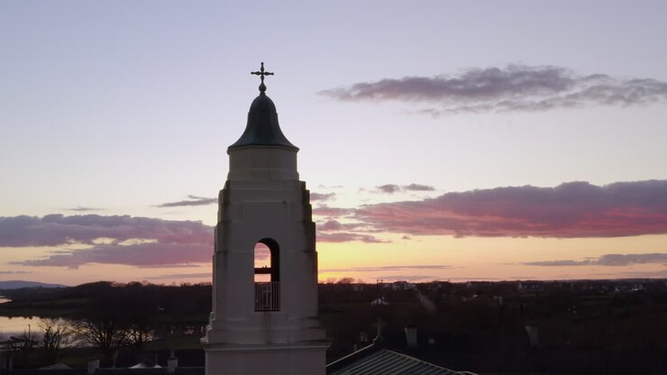 Medium aerial orbit of historic Clarinbridge church framed by vibrant sunset sky and warm colors
