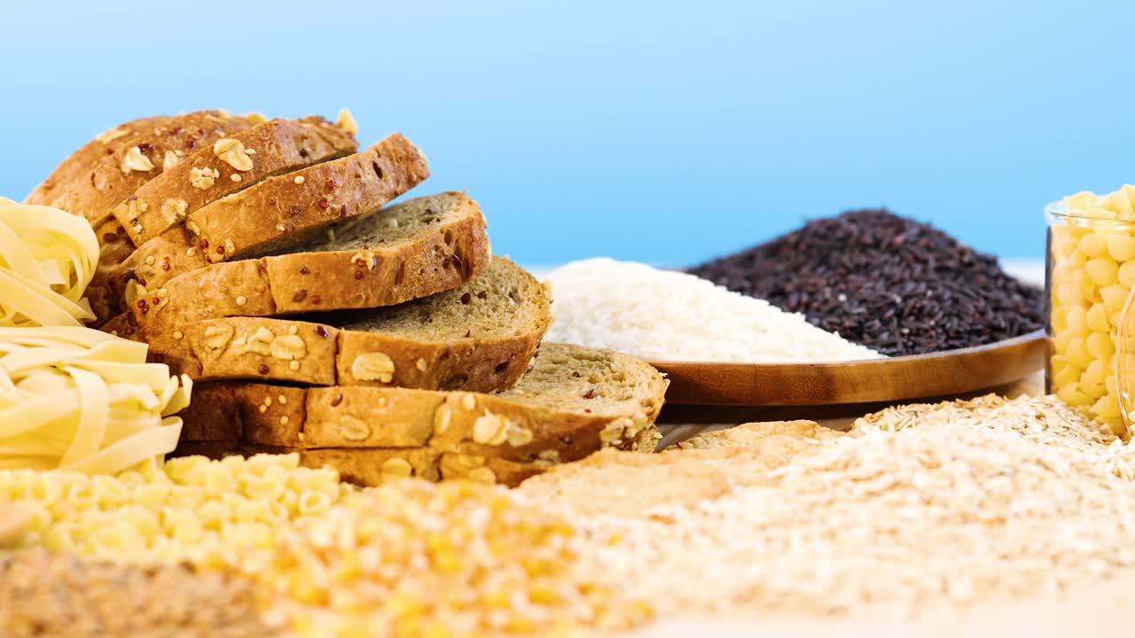 A variety of grains, pasta, and bread arranged against a bright blue background, highlighting texture and color