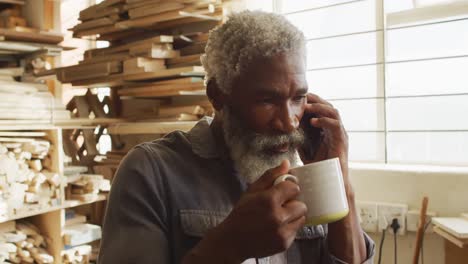 carpintero afroamericano hablando en un teléfono inteligente en una carpintería