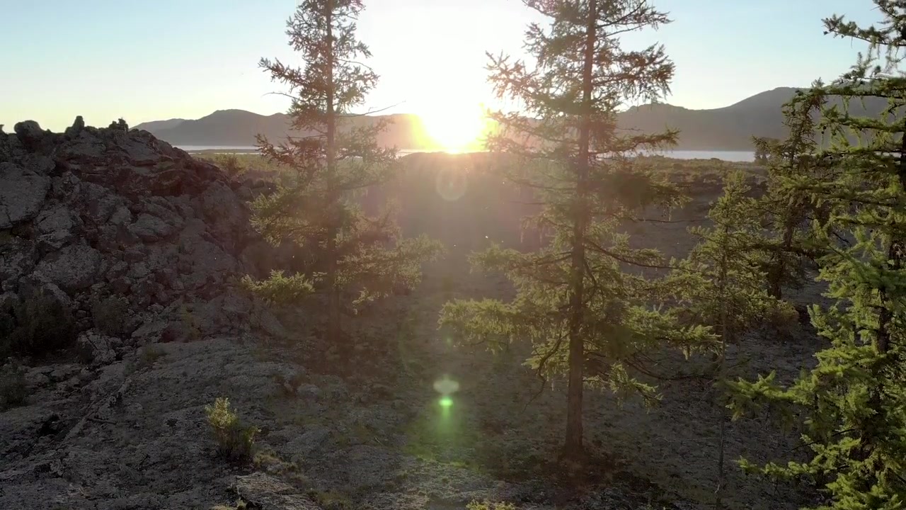 Auringonlasku kivikkoisen maiseman yllä havupuiden kera