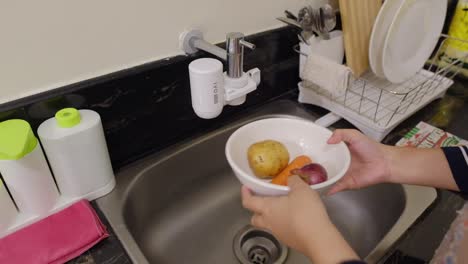 disparo en primer plano de manos lavando verduras en un tazón debajo del grifo del fregadero de la cocina