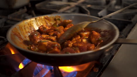 Spoon-stirs-paneer-masala-in-stainless-skillet-over-commercial-stove,-close-up-slow-motion-HD