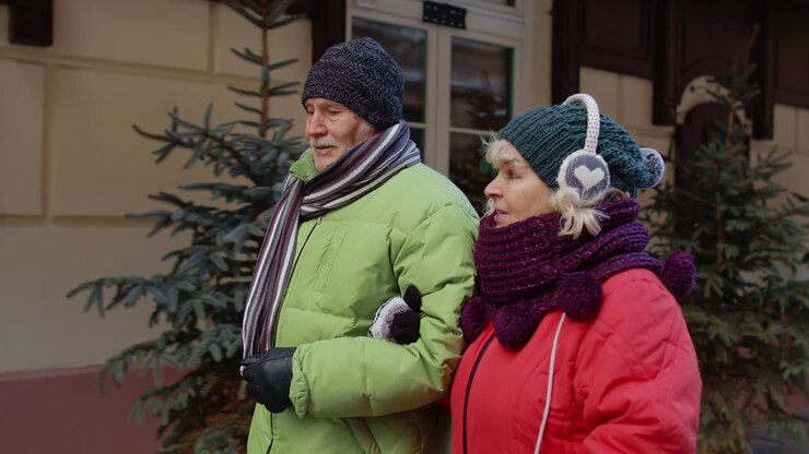 Vista frontale di una coppia di turisti anziani (uomo e donna) che camminano, parlano e gesticolano in una città durante le vacanze invernali