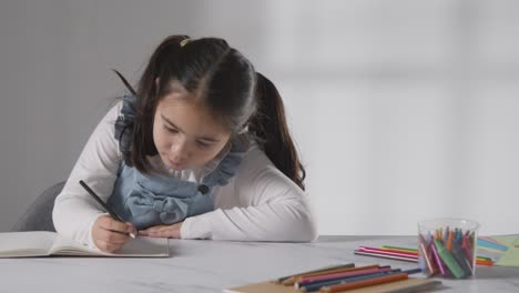 Foto-De-Estudio-De-Una-Joven-En-La-Mesa-Escribiendo-En-Un-Libro-Escolar