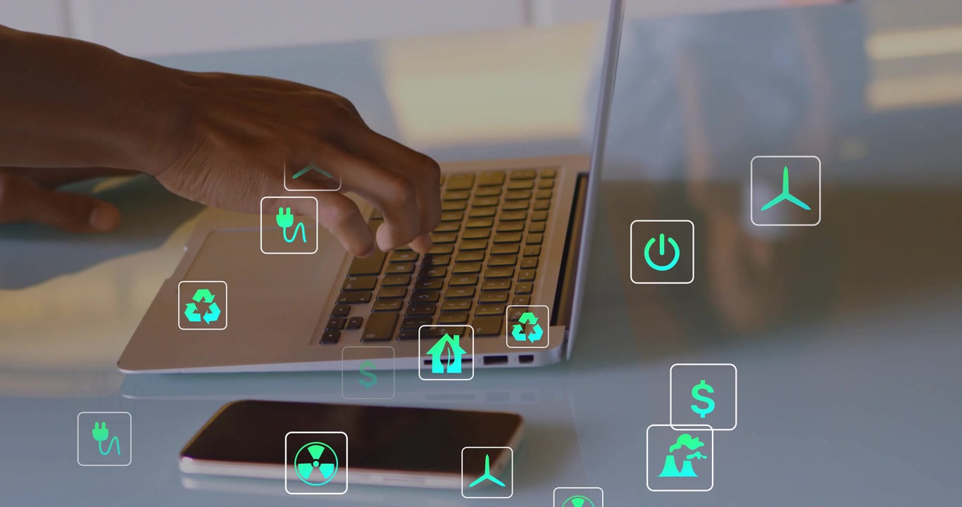 Male hand typing on laptop analyzing energy and finance while generating green icons above phone